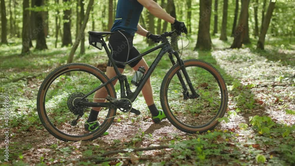 A cyclist is walking with a bicycle along a forest path. He is wearing bicycle clothing. The camera is focused on the bike. 4K A cyclist is walking with a bicycle along a forest path. He is wearing bicycle clothing. The camera is focused on the bike. 4K