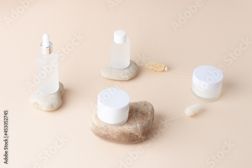 Cosmetic skin care products with flowers and stones on pastel beige background. Close up