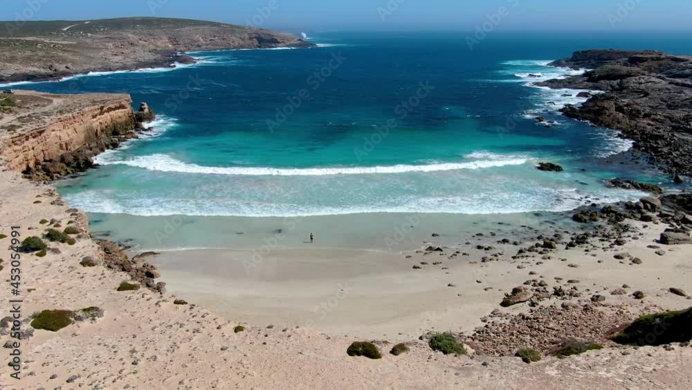 Man alone in the middle of a paradise beach with white sand and turquoise water watching the waves coming. Aerial shot from a drone. Man alone in the middle of a paradise beach with white sand and turquoise water watching the waves coming. Aerial shot from a drone.