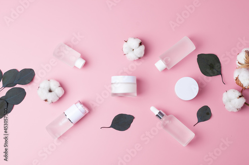 Cosmetic skin care products with flowers and eucalyptus on pink background. Flat lay, copy space