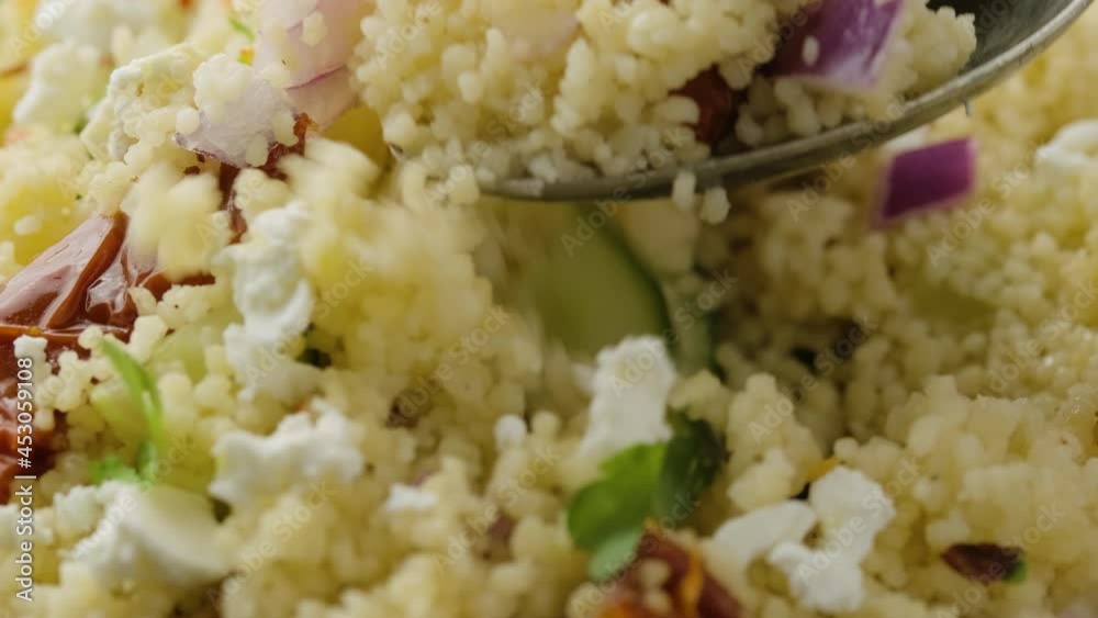 Picking Couscous salad with sun dried tomatoes, cucumber, red onion and feta cheese using a tablespoon. healthy food. Picking Couscous salad with sun dried tomatoes, cucumber, red onion and feta cheese using a tablespoon. healthy food.