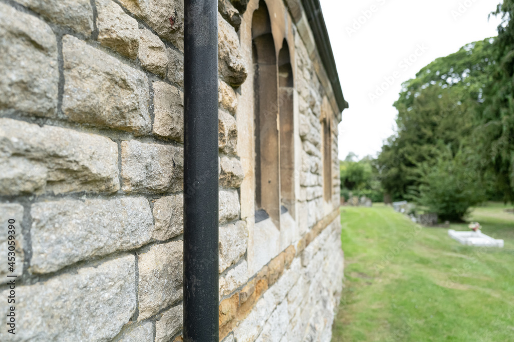 Detailed view of the side of a famous English church showing the textured stone wall construction. A wrought Iron drainpipe and large cemetery is also in view.