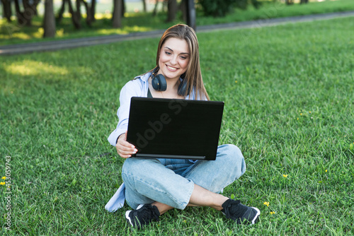A young and attractive girl in headphones sitting on the grass on the lawn. Diastance working. Freelance, blogging concept