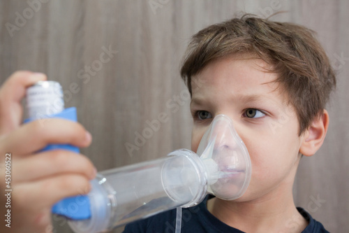 Child boy using medical spray for breath. Inhaler, spacer and mask. Side view photo