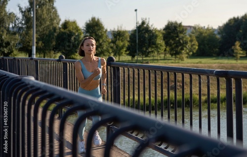 A fit young caucasian woman running intensively in slow motion on the bridge in the morning. Concept of a healthy lifestyle. Long shot of running woman. Vitality of sport. 