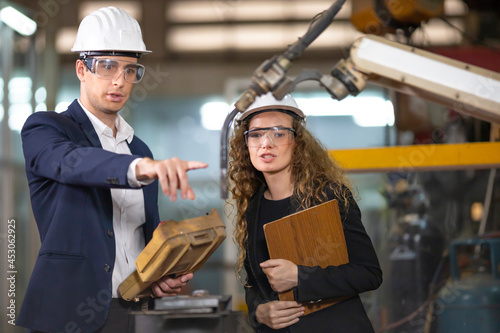 Two Caucasian engineers are inspecting the welding robot machine arm inside mechanic factory photo