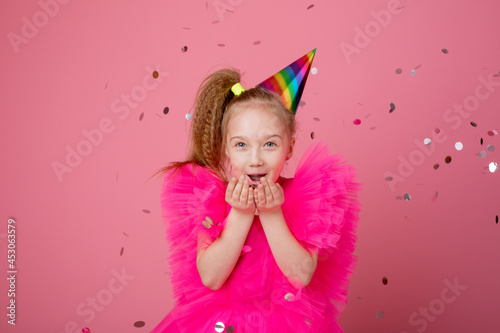 a little girl on a pink background blowing confetti celebrates her birthday