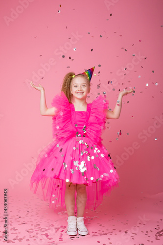 a little girl on a pink background catches confetti celebrates her birthday