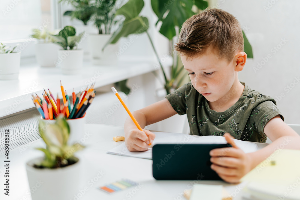 Back to school. Distance learning online education. Caucasian smile kid boy studying at home with mobile smart phone and doing school homework. Thinking child with cellphone, pencil and training books Back to school. Distance learning online education. Caucasian smile kid boy studying at home with mobile smart phone and doing school homework. Thinking child with cellphone, pencil and training books