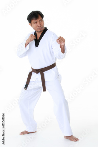 Isolated portrait studio shot of Asian middle aged male tae kwan do karate judo sport athlete in uniform with brown belt standing look at camera posing strong gesture in front of white background