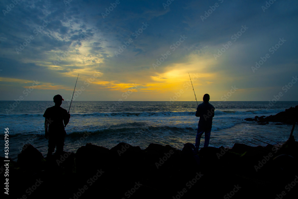 Two people fishing during the sunset on the beach, Silhouetted photography