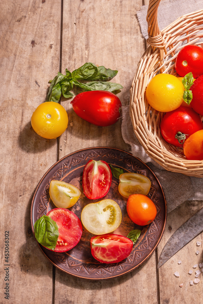 Ripe assorted tomatoes with fresh basil in a wicker basket Ripe assorted tomatoes with fresh basil in a wicker basket