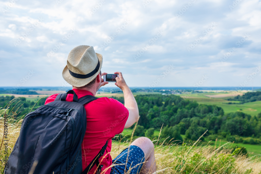 Young male tourist photographs with telephone camera the landscape of the mountain on a camping summer tour. Young male tourist photographs with telephone camera the landscape of the mountain on a camping summer tour.