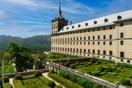 View of the San Lorenzo de el Escorial in Madrid, with gardens in the foreground and blue sky with light white clouds.