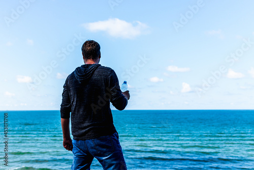 Middle age man relaxing and holding water bottle on the beach after promenade at summer day.Copy space.