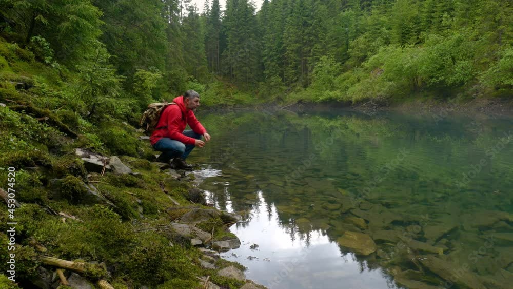 A bearded man with a backpack drinks water from a clean lake A bearded man with a backpack drinks water from a clean lake