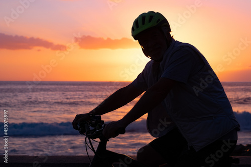 Silhouette of mature man riding his bicycle at the beach at sunset. Horizon over water