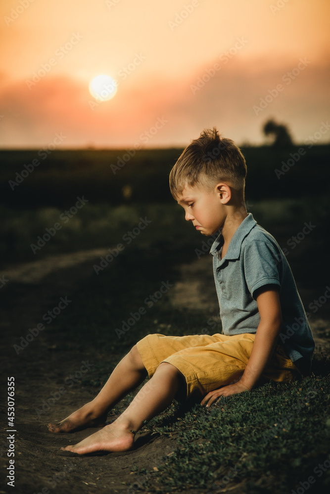 little boy sitting at sunset and crying