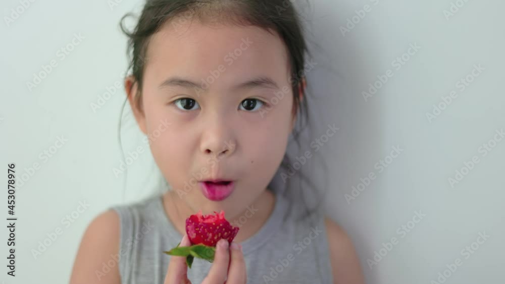 Young Asian girl holding a large strawberry eating deliciously with white background. Young Asian girl holding a large strawberry eating deliciously with white background.