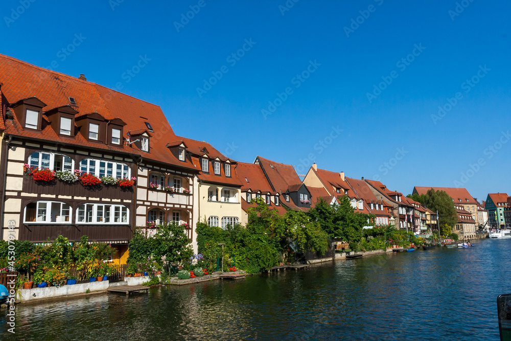 Bamberg Germany 08-08-2019 - Picturesque view of the medieval buildings along the Regnitz River with old barge, moored boats and on the river shore in UNESCO Heritage city Bamberg, Bavaria, Germany.