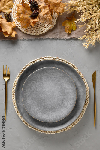 Halloween and Thanksgiving day table setting with gray plate as mockup decorated fallen leaves,natural materials on gray table. Festive dinner. Top view. Vertical format.