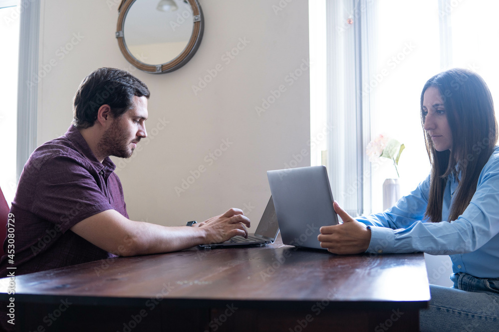 Man and woman working at home at the table in front of each other. Remote work, freelance, modern lifestyle.