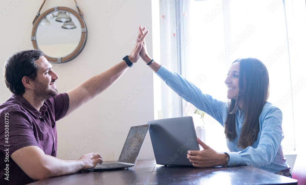 High- five! An attractive couple giving each other a successful high-five while working from home as a symbol of achieving goals and ambitions. `Supporting each other