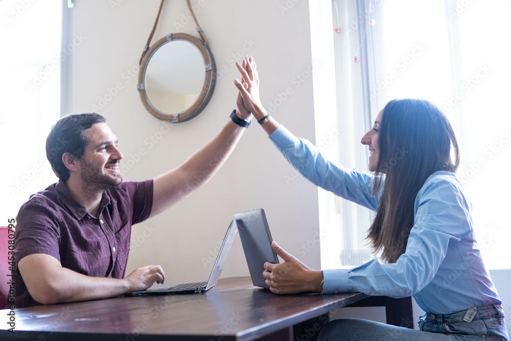 High- five! An attractive couple giving each other a successful high-five while working from home as a symbol of achieving goals and ambitions. `Supporting each other