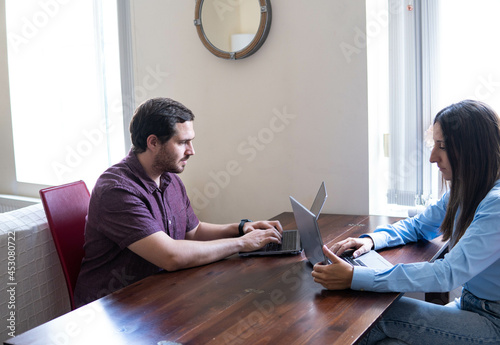 Obraz na płótnie Man and woman working at home at the table in front of each other. Remote work, freelance, modern lifestyle.
w salonie