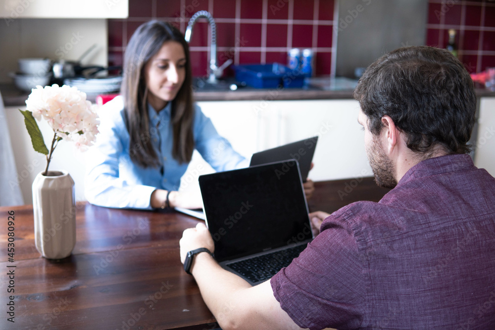 Man and woman working at home at the table in front of each other. Remote work, freelance, modern lifestyle.