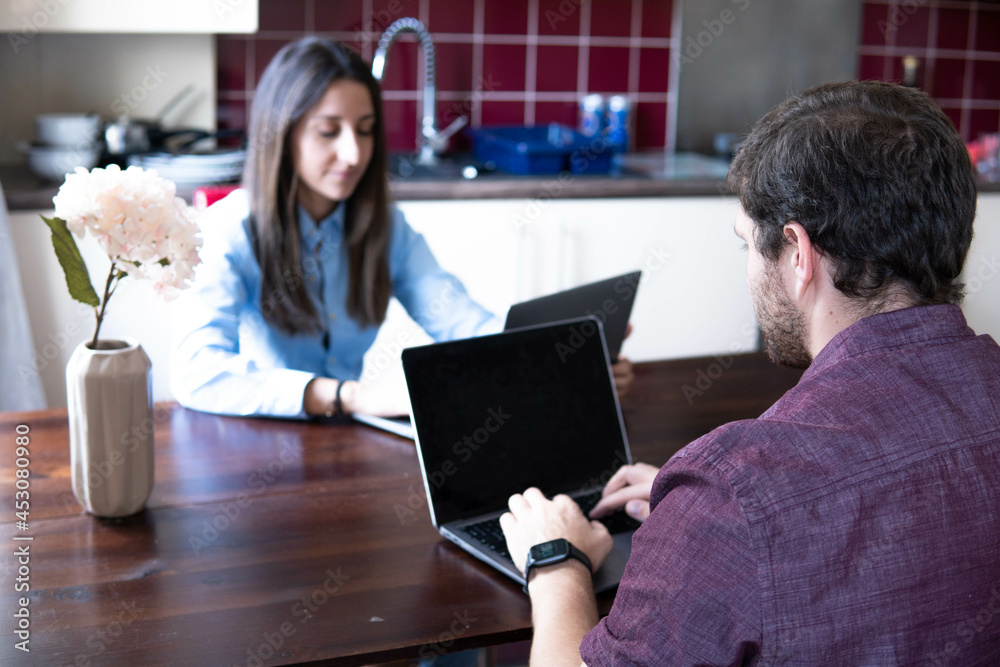 Man and woman working at home at the table in front of each other. Remote work, freelance, modern lifestyle.