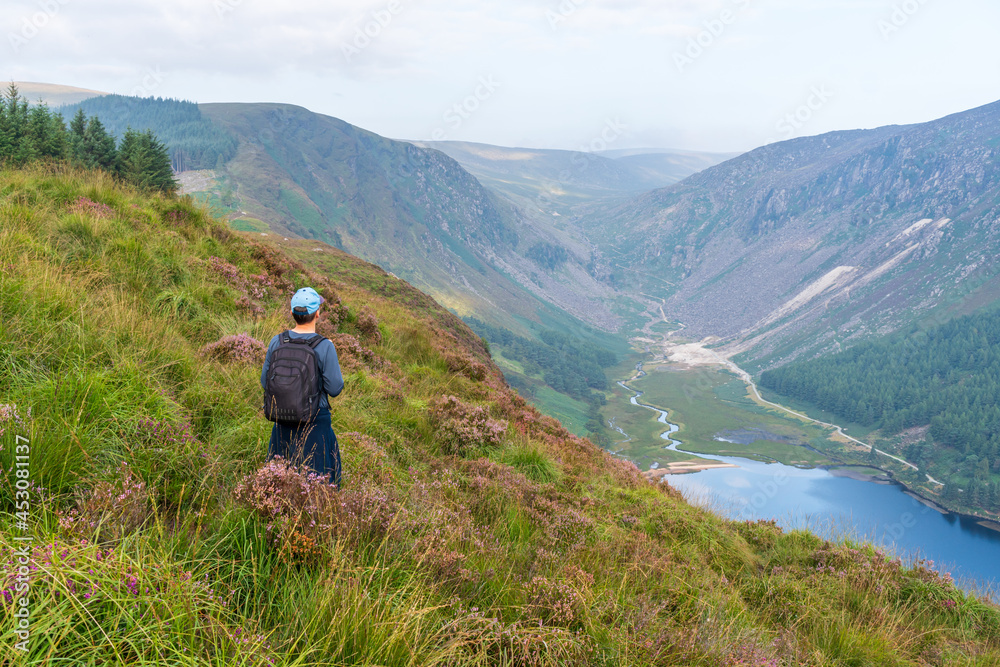 Young man admiring the view over the Glendalough Lake and Glenealo Valley, in Wicklow Mountains, Ireland, after hiking a segment of the popular Spinc trail.