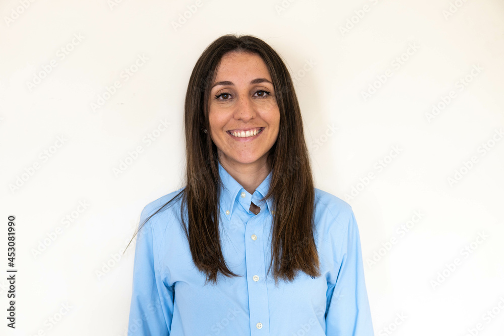 Young and attractive woman looking corporative with a shirt smiling at the camera, looking professional and ready to do bussiness with a white background. Wearing a blue shirt. Latin woman business.