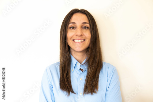 Obraz na płótnie Young and attractive woman looking corporative with a shirt smiling at the camera, looking professional and ready to do bussiness with a white background. Wearing a blue shirt. Latin woman business. w salonie