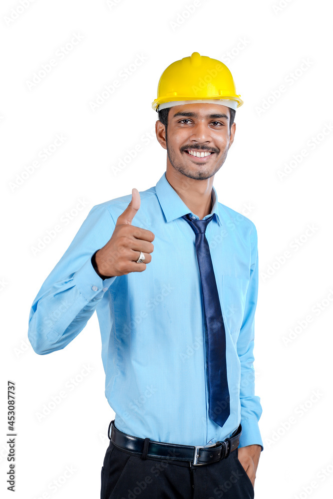 Young Indian engineer wearing yellow color hard hat and giving successful gesture.