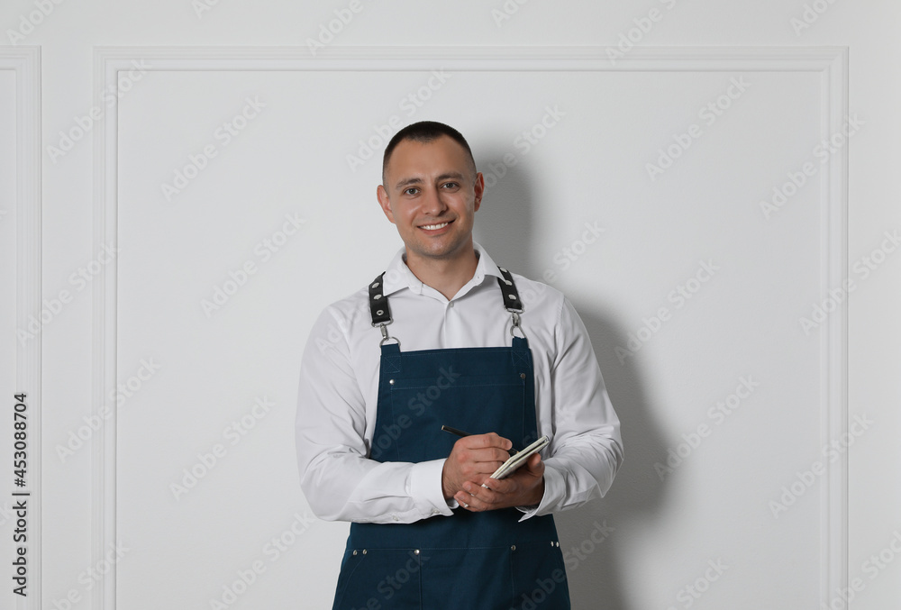 Portrait of happy young waiter with notebook near white wall Portrait of happy young waiter with notebook near white wall