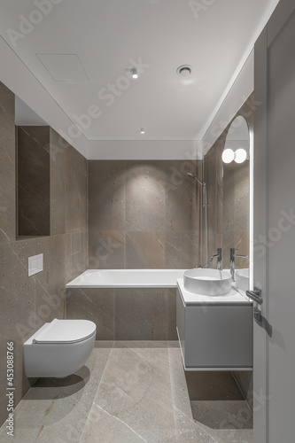 Modern minimalist bathroom beige interior design with marble tiles and beige furniture.