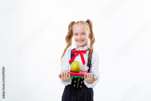  little girl in a school uniform holds a book and an apple isolated on a white background