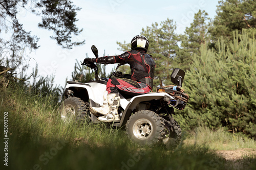 Man driving modern quad bike on sandy road near forest. Extreme sport