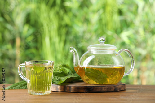 Aromatic nettle tea and green leaves on wooden table outdoors
