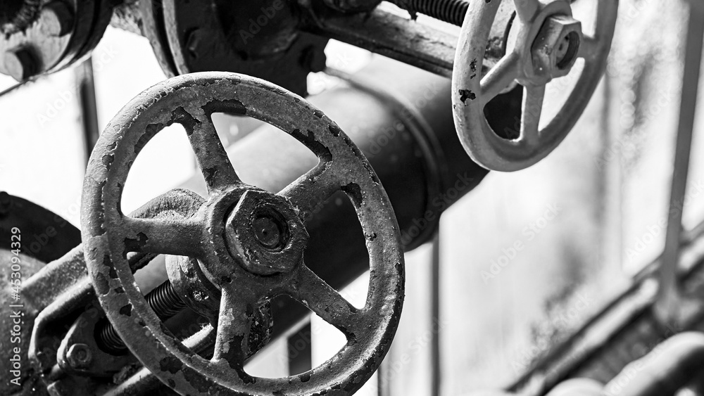 Two old grunge steampunk valve wheels selective focus with handle grip over out of focus industrial metal BW background 16x9 with copyspace in black and white.