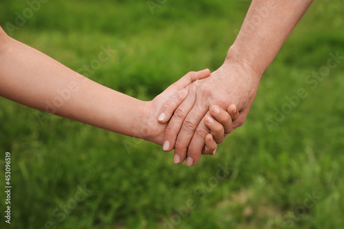 Little girl and grandmother holding hands together in park, closeup