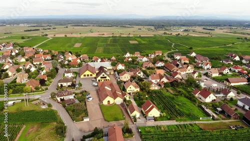 Modern houses and buildings, residential estate and wineries of Orschwiller village. Aerial shot of small Alsace town, camera fly back. Green fields of vineyards seen on background