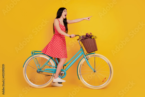 Profile portrait of lady ride bicycle indicate finger empty space wear red short dress sneakers on yellow background photo