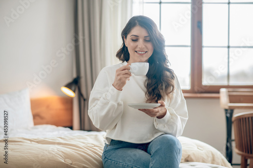 Pretty young woman sitting on the bed and drinking coffee