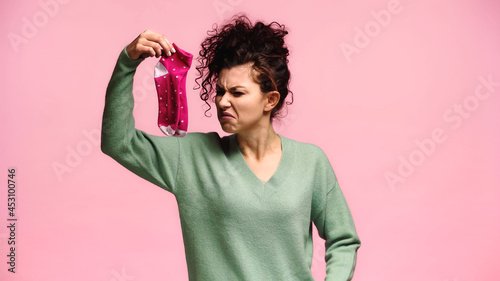 woman feeling disgusted while holding smelly socks isolated on pink