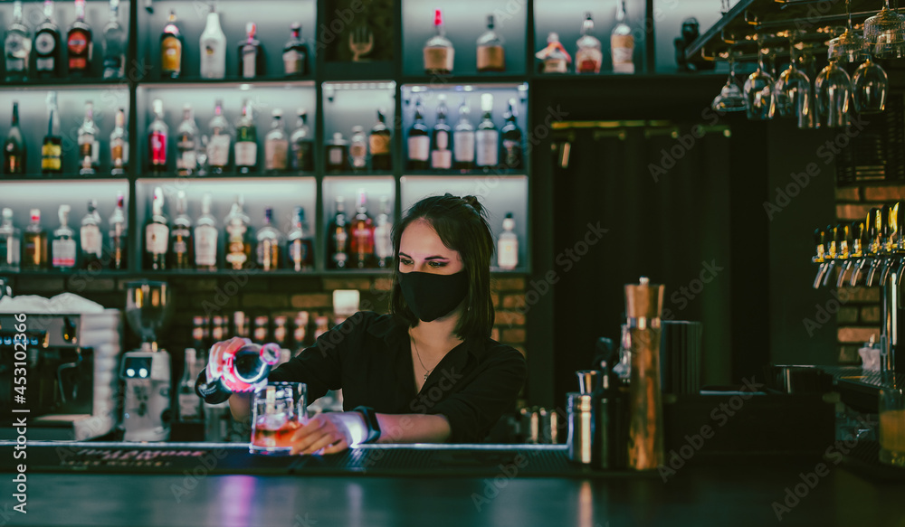 Portrait of young attractive woman bartender with mask Making Cocktail in bar