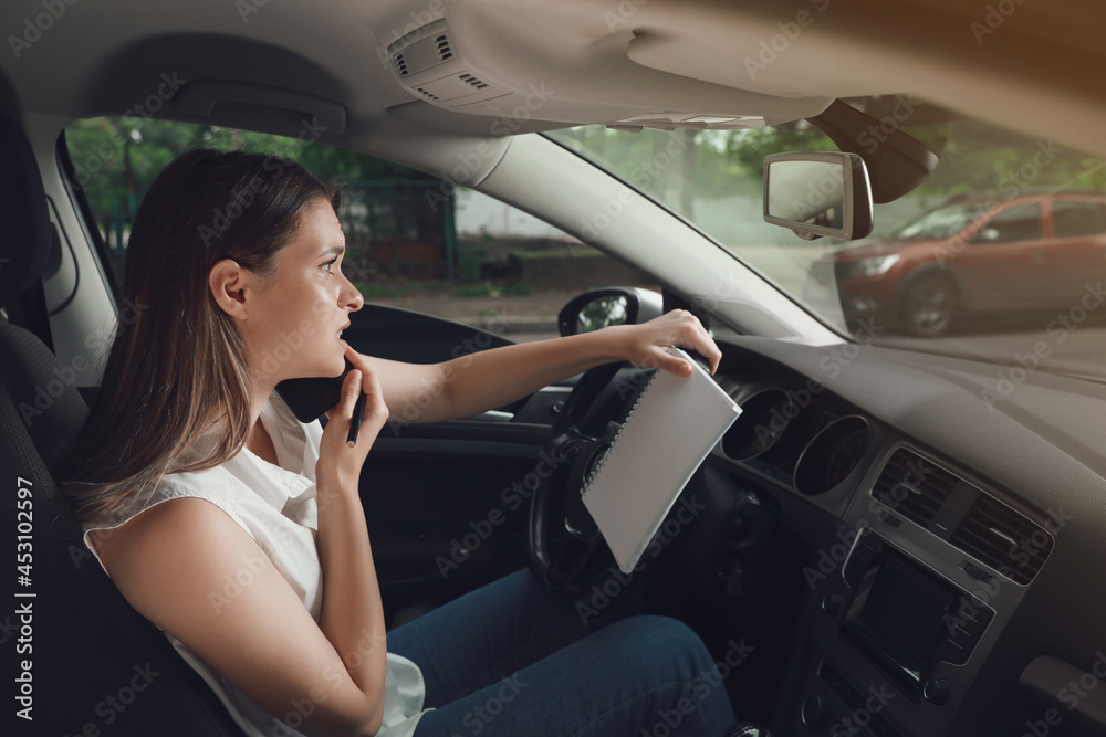 Stressed young woman with notebook talking on phone in driver's seat of modern car Stressed young woman with notebook talking on phone in driver's seat of modern car