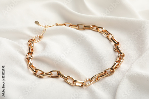 Fotografija Elegant golden necklace on white fabric. Stylish bijouterie