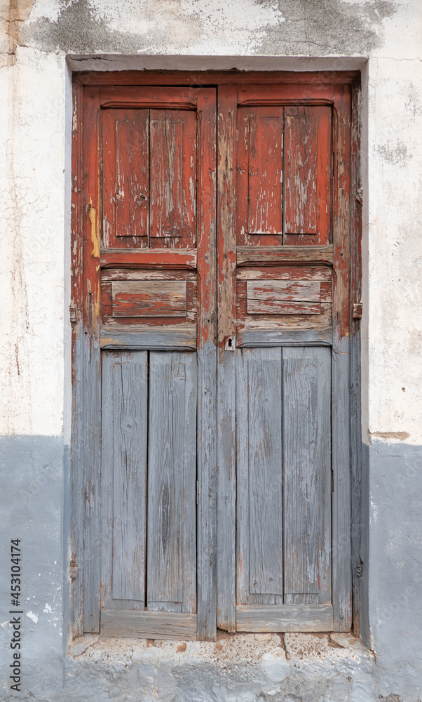 Alte, stark verwitterte, grau rote Tür aus Holz, Detail in einer heruntergekommenen Fassade  